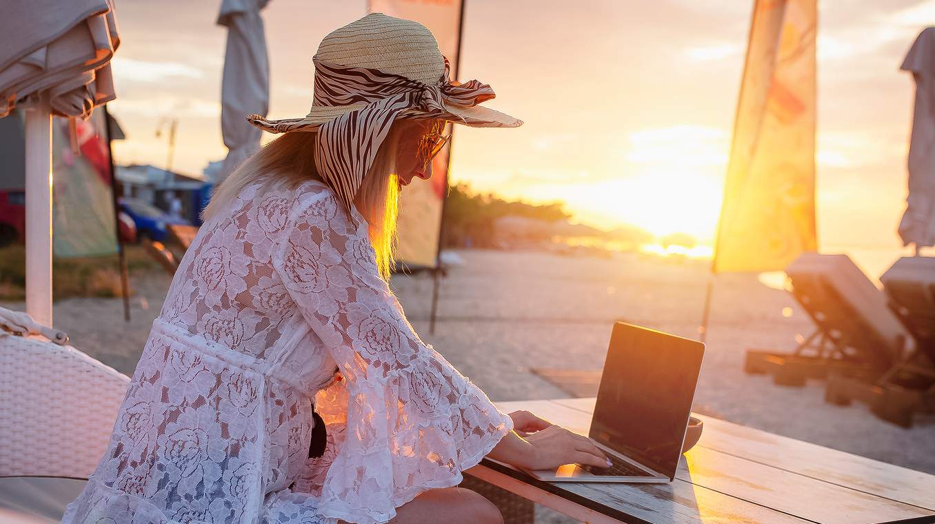 A woman working on a laptop on the beach as the sun sets